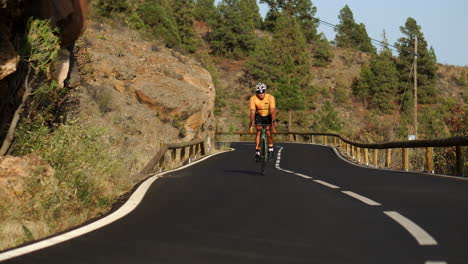 A-guy-wearing-a-yellow-t-shirt-is-cycling-on-a-sports-road-bicycle-along-a-road-situated-at-a-high-elevation-in-the-mountains